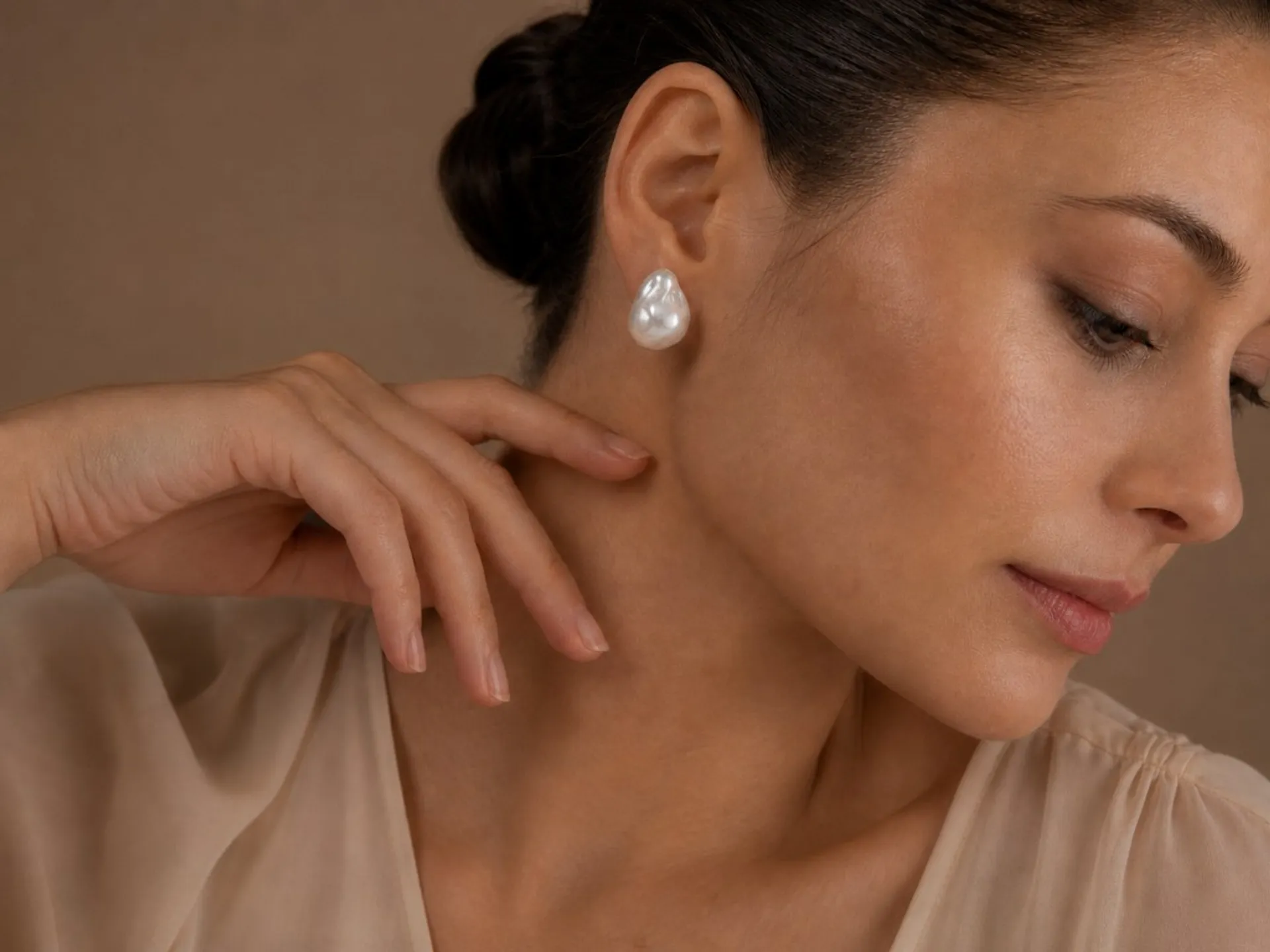 Woman in profile wearing a large baroque pearl earring, warm neutral studio light