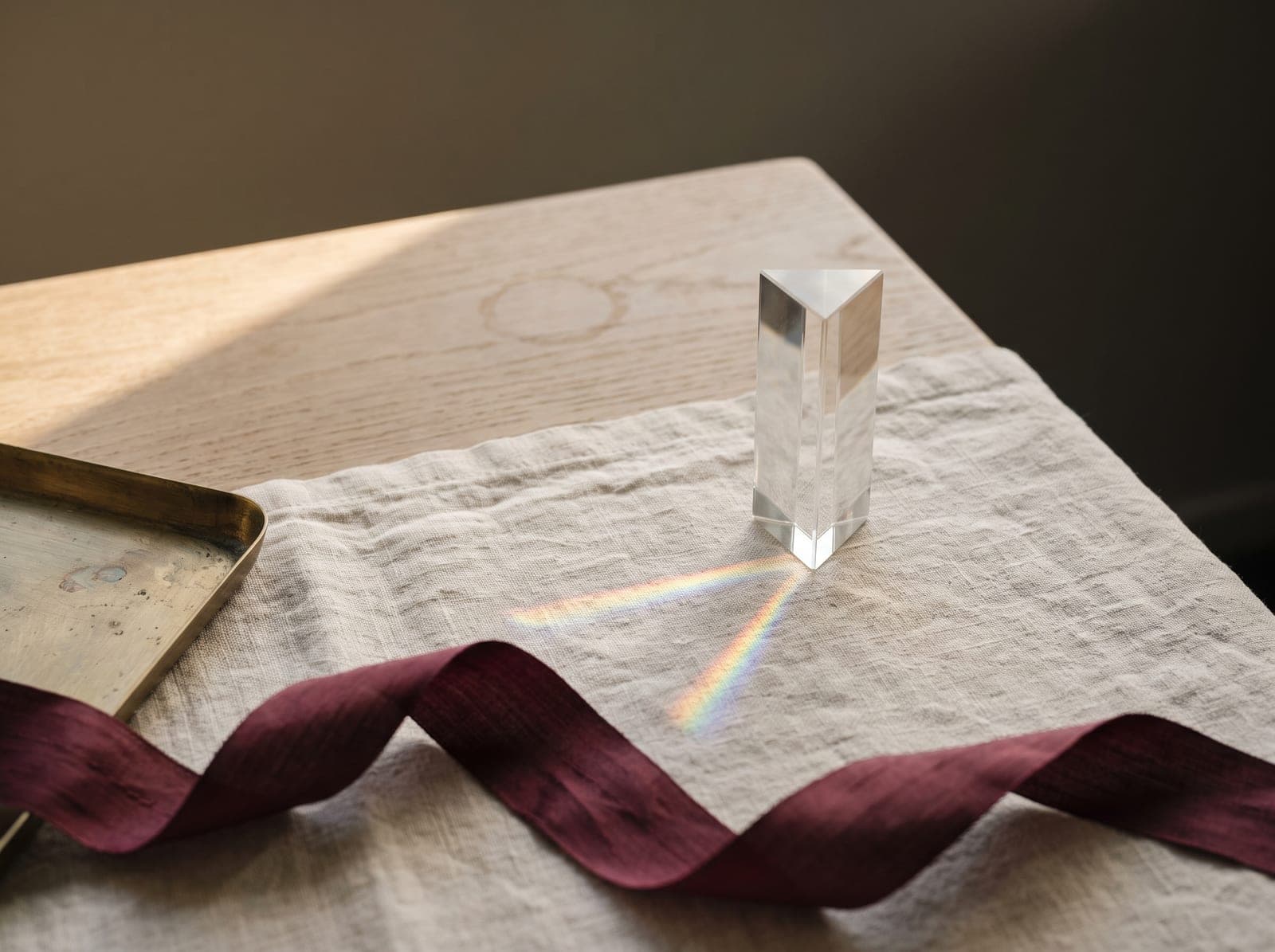 A glass prism casting a small rainbow across cream linen in warm window light